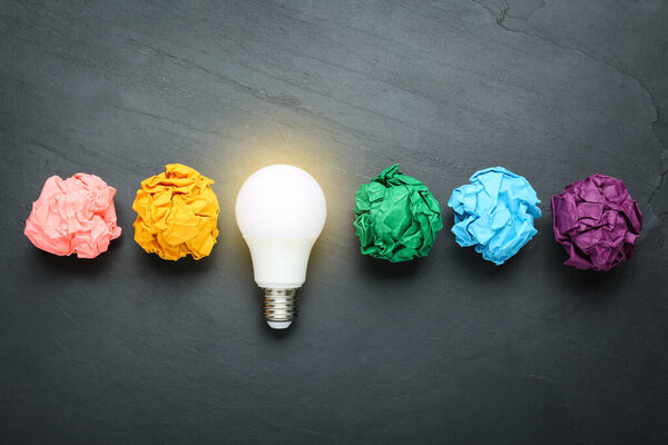 Creative flat lay composition with lightbulb and colorful paper balls on black table. Idea concept