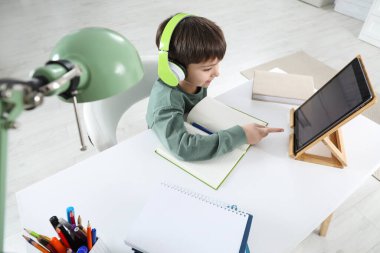 Modern tabletle evde internetten ders çalışan şirin bir çocuk. E-öğrenme