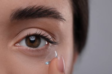 Gri arka plana kontak lens takan genç kadının yakın görüntüsü