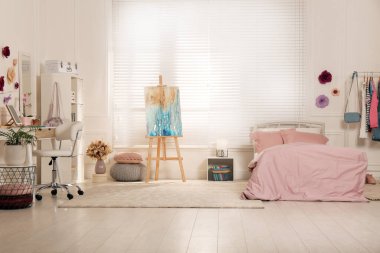 Şık bir gencin odası, içi bilgisayar, rahat yatak ve resim sehpası.