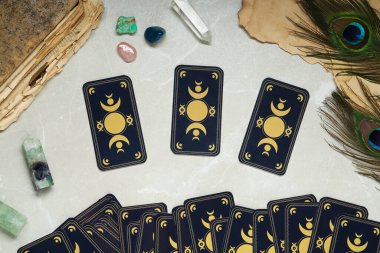 Tarot kartları, tavus kuşu tüyleri, değerli taşlar ve ışık masasında duran eski kitaplar, düz yataklar. Ters taraf