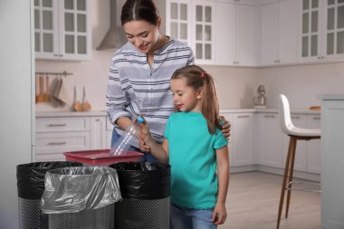 Genç kadın ve kızı mutfaktaki çöp kutusuna plastik şişe atıyorlar. Atık toplamayı ayır