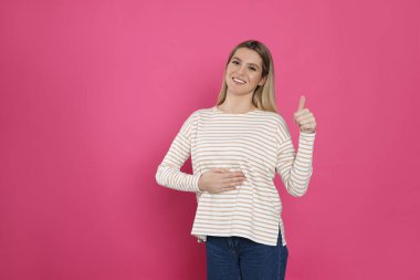 Mutlu kadın göbeğine dokunuyor ve pembe arka planda baş parmağını gösteriyor, mesaj için yer var. Sağlıklı mide kavramı