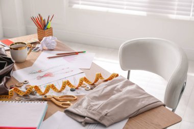 İçerideki ahşap masada giysi çizimleri ve farklı eşyalar. Moda tasarımcısının işyeri