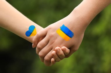 Ukrayna 'daki savaşı durdurun. Anne ve çocuğu el ele tutuşuyor, açık havada yakın çekimde. Ukrayna bayrağı renginde çizimler