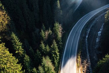 Güneşli bir günde asfalt yolun havadan görünüşü kozalaklı ormanlarla çevrilidir. Drone fotoğrafçılığı