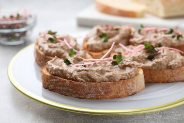 Lezzetli ezmeli ekmek dilimleri ve açık gri masada mikroyeşiller, yakın plan.