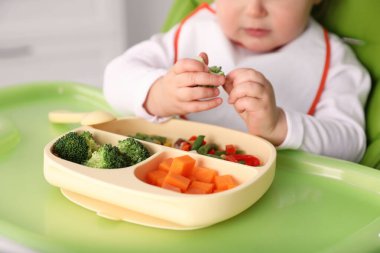 Küçük bebek yüksek sandalyede yemek yiyor, yakın plan.