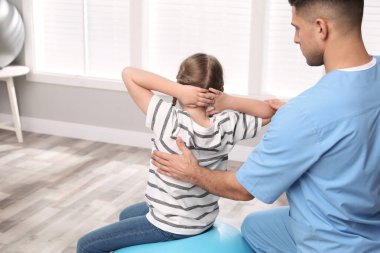 Ortopedist, çocuğun klinikte egzersiz yapmasına yardım ediyor. Skolyoz tedavisi
