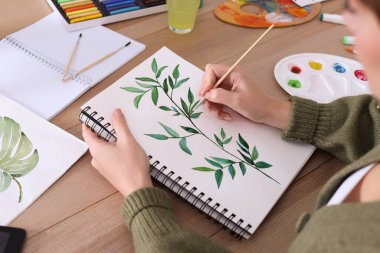 Ahşap masadaki çizim defterine yeşil dal çizen kadın, yakın plan.