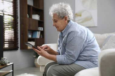 Oturma odasında tablet kullanan kötü duruşu olan yaşlı bir kadın.