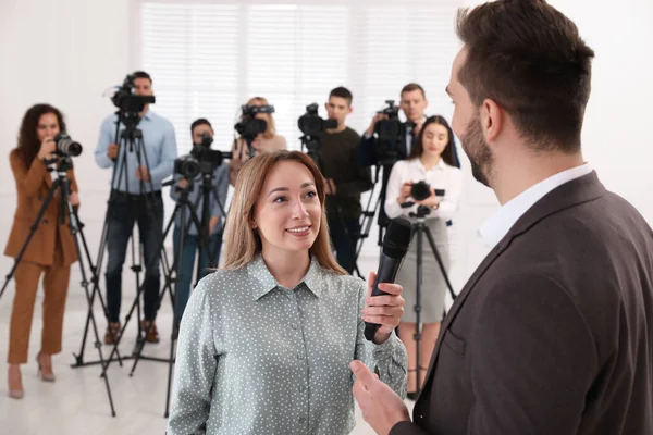 Professional young journalist interviewing businessman and group of video camera operators on background