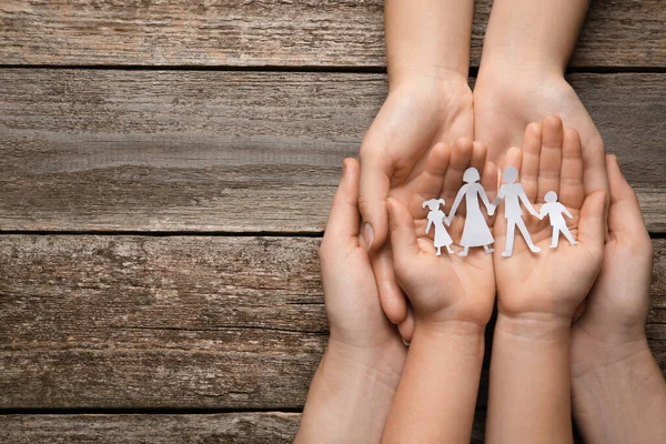 Parents and child holding paper cutout of family at wooden table, top view. Space for text