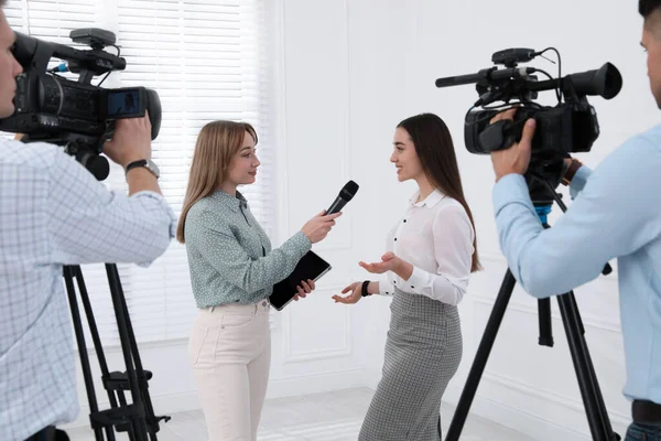 Professional journalist interviewing young business woman and cameramen shooting video for broadcast