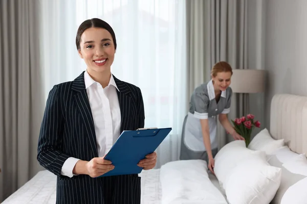 Housekeeping manager with clipboard checking maid\'s work in hotel bedroom