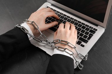 İnternet bağımlılığı. Siyah masada elleri zincirli bir şekilde dizüstü bilgisayarda yazan adam.