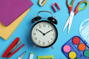 Alarm saati ve açık mavi zemin üzerinde farklı kırtasiye malzemesi olan düz bir kompozisyon. Okul zamanı.