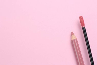 Pembe arka planda parlak dudak kalemi ve sıvı ruj fırçası, metin için yeri olan düz bir yer. Kozmetik ürünleri