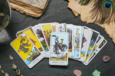 Tarot kartları, eski kitaplar, kristaller ve tavus kuşu tüyleri siyah masada, düz yatıyordu.