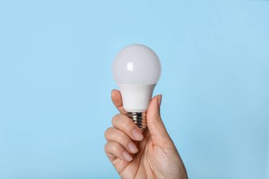 Mavi arka planda LED ampulü tutan kadın, yakın plan