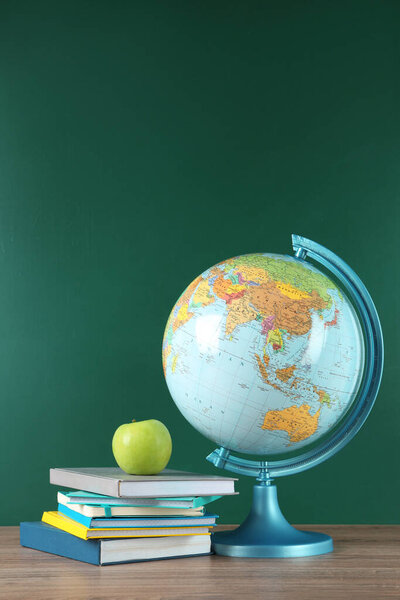 Globe, books and apple on wooden table near green chalkboard. Geography lesson
