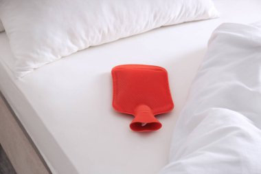 Beyaz yatakta kırmızı sıcak su şişesi.