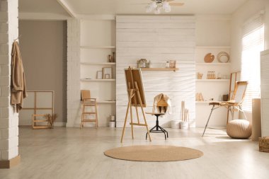 Sanatçının iş yeri ve geniş pencerenin yanında katlanabilir ahşap sehpası olan modern bir stüdyo.