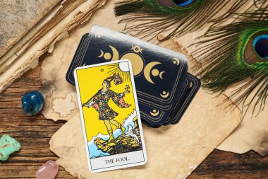 Tavus kuşu tüyleri, değerli taşlar ve ahşap masa üzerindeki eski kitaplarla dolu diğer tarot kartlarının yanındaki aptal.