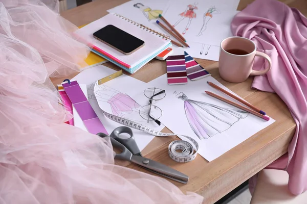 Sketches of clothes and different stuff on wooden table. Fashion designer's workplace