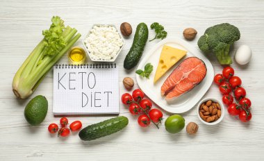 Keto Diyet cümlesi ve beyaz ahşap masa üzerinde farklı ürünler içeren defter, düz yatıyordu