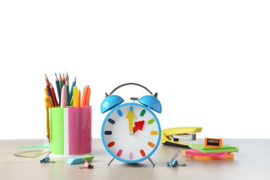 Açık mavi alarm saati ve ahşap masada beyaz arka plana karşı farklı kırtasiye malzemesi. Okul zamanı.