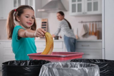 Küçük kız mutfaktaki çöp kutusuna muz kabuğu atıyor. Atık toplamayı ayır