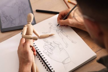 Çizim defterinde manken çizen adam, ahşap masadaki kalemle yakın plan.