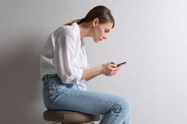 Kvinna Med Dålig Hållning Med Smartphone Medan Sitter Pall Mot — Stockfoto