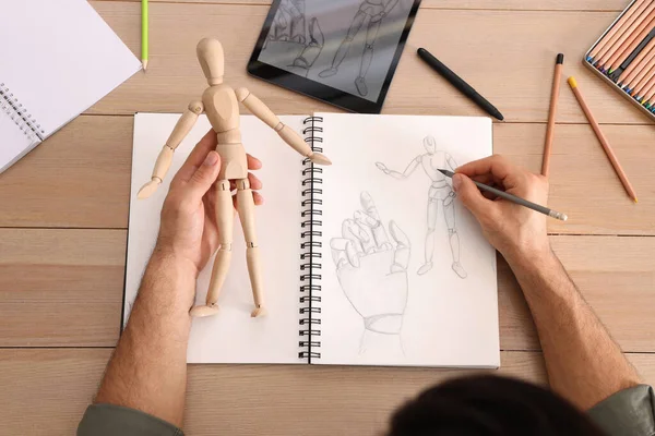 男は木製のテーブルで鉛筆でスケッチブックでマネキンを描く トップビュー — ストック写真