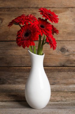 Tahta masadaki seramik vazoda güzel kırmızı gerbera çiçekleri.