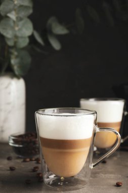 Cam fincanlar lezzetli latte macchiato ve dağınık kahve çekirdekleri gri masada.