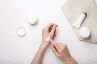 Beyaz ahşap masada bileğine vücut kremi süren bir kadın.