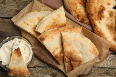 Tahta masanın üzerinde taze pita ekmek ve krem peynir parçaları.