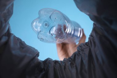 Açık mavi arka planda plastik şişeyi çöp kutusuna atan kadının alt görüntüsü, yakın plan.