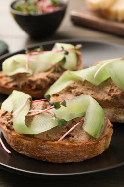 Lezzetli ezmeli ekmek dilimleri, salatalık ve mikro yeşiller masada, yakın plan.