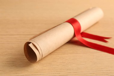Mezuniyet diploması, ahşap masada kırmızı kurdeleyle bağlanmış, yakın plan.