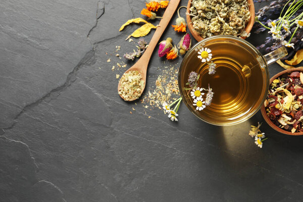 Glass cup of aromatic freshly brewed tea near different dry herbs on black table, flat lay. Space for text