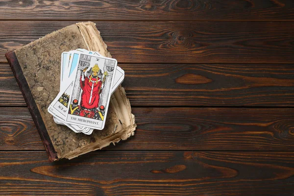 Tarot cards with old book on wooden table, top view. Space for text