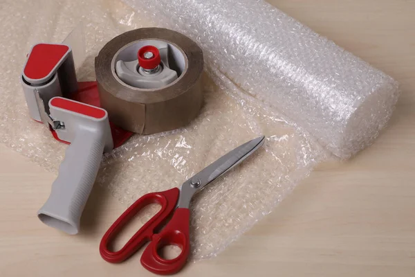 Roll of bubble wrap, scissors and adhesive tape on wooden table