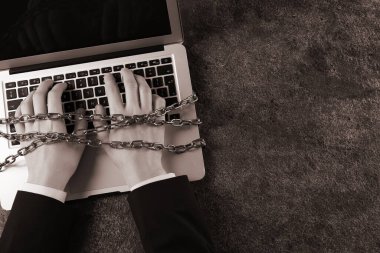 Gri masada dizüstü bilgisayar kullanan elleri zincirli internet bağımlısı bir kadın. Mesaj için yer var. Sepya etkisi
