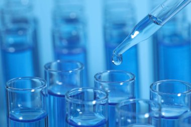 Açık mavi arkaplanda test tüpüne reaktör damlatılıyor, yakın plan ve metin için boşluk. Laboratuvar analizi