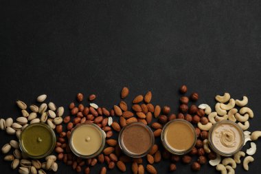 Farklı fındık ve malzemelerden yapılmış tereyağlı kavanozlar siyah masada, düz yerde. Metin için boşluk