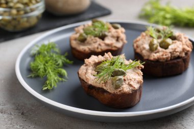 Lezzetli ezmeli ekmek dilimleri, kapari ve dereotu açık gri masada, yakın plan.
