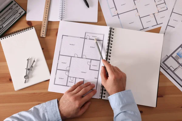 Ahşap masada çizim defteri ve kalemi olan bir adam.